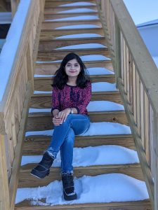 Industrial engineering graduate student Gazi Nazia Nur sits on some snow-covered stairs. She is wear blue jeans and a pink/purple shirt.