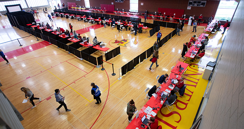 An overhead shot of a COVID-19 vaccination clinic set up inside of State Gym. Faculty and staff members help students to check in as they go through the line to get their shot.