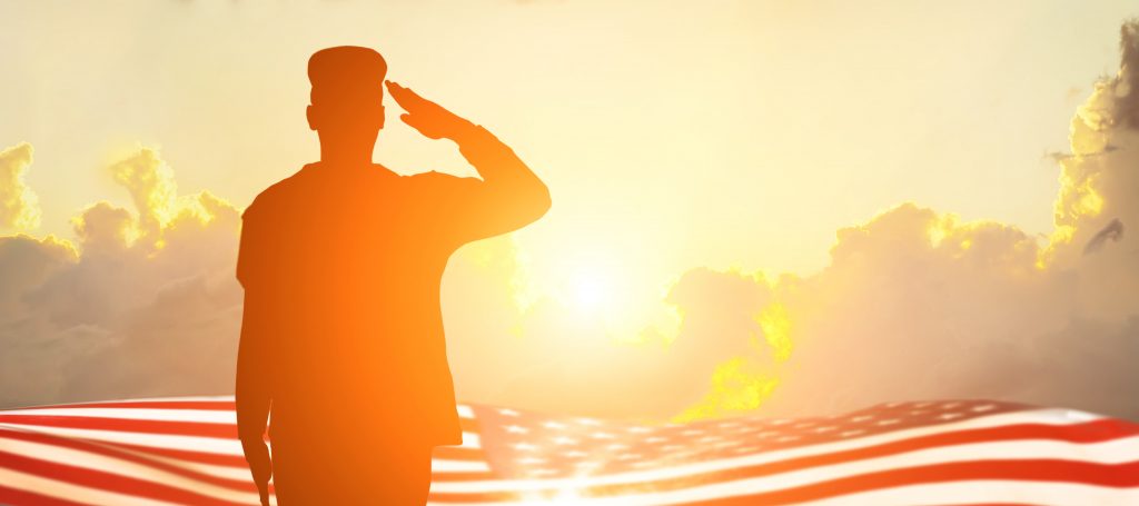 A solider salutes with an American flag and sunrise in the background