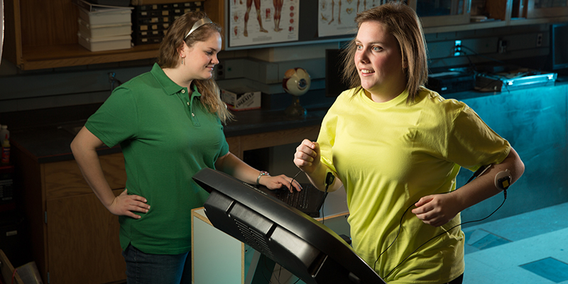 A student runs on a treadmill while another students analyzes data