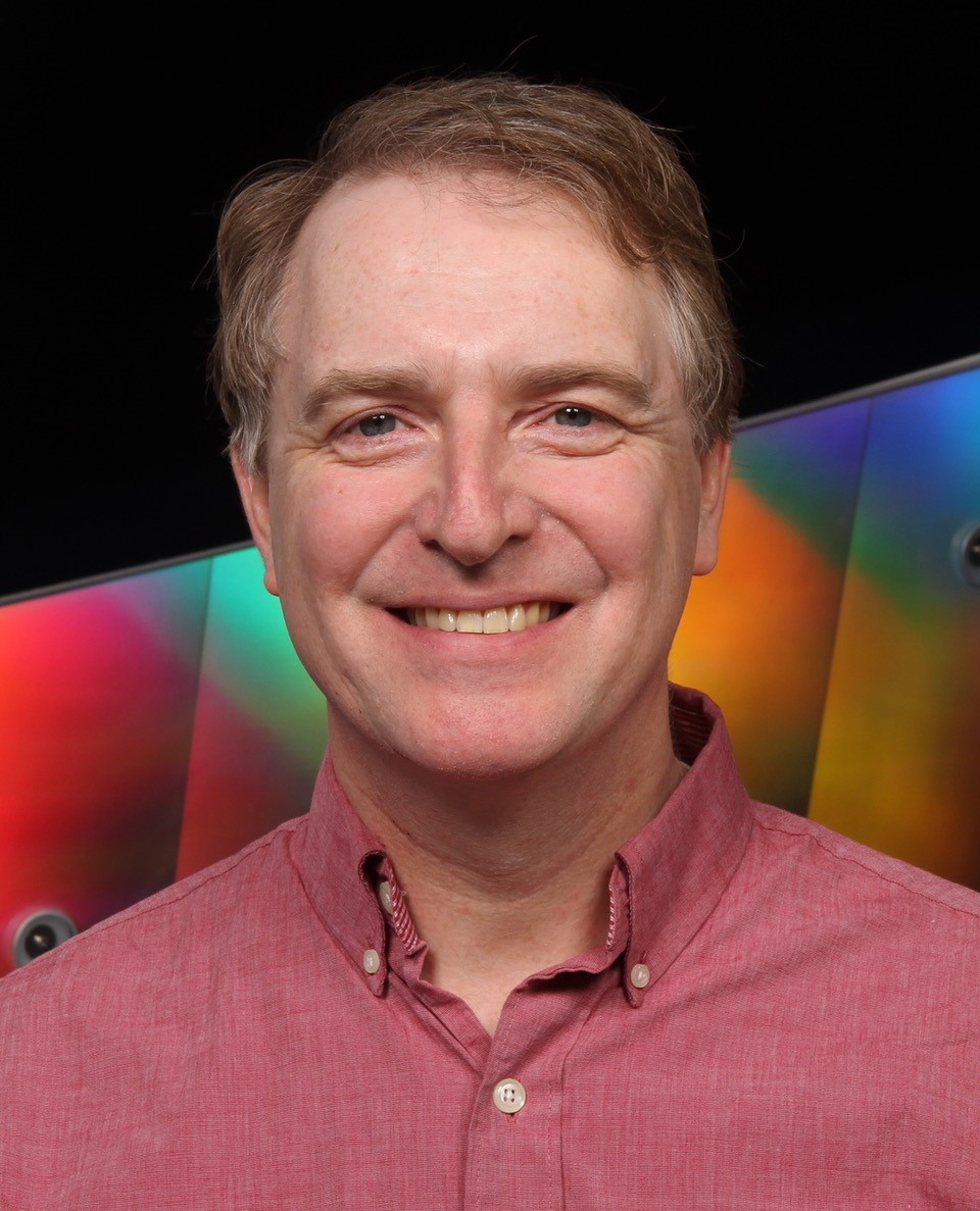 Stephen Gilbert smiles and wears a red collared shirt.